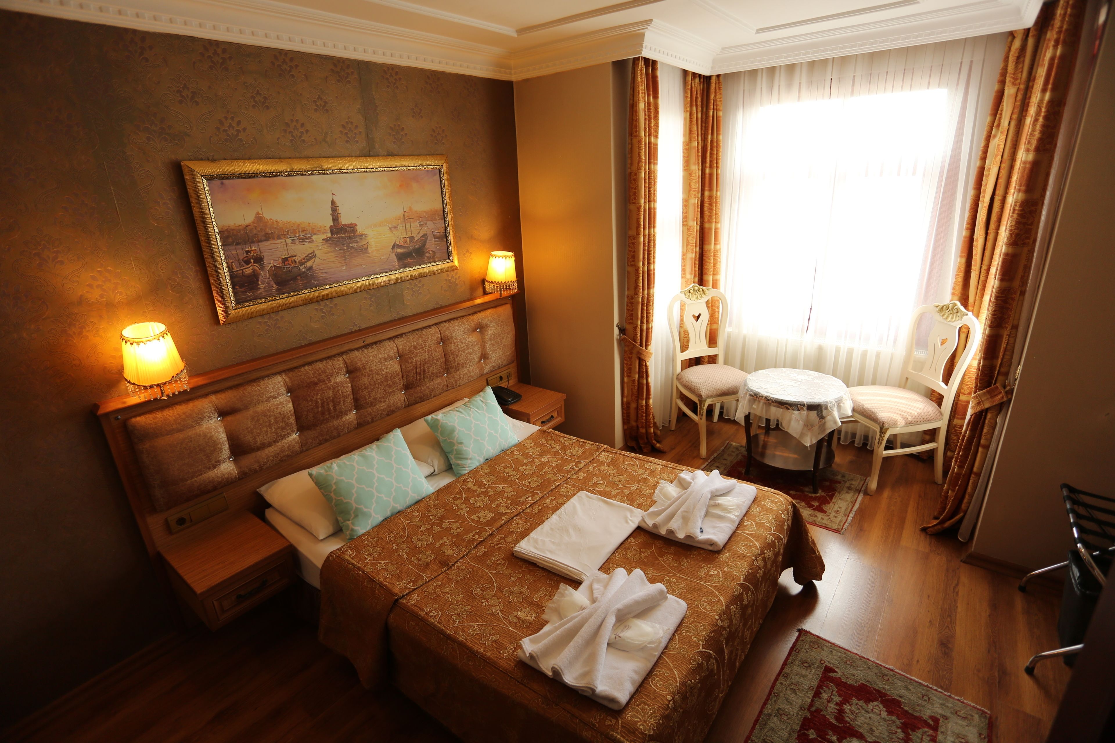 Une chambre d’hôtel avec un grand lit, une table de chevet, une commode, une chaise, une petite table et un tableau au mur.
