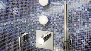 Un baño con pared de mosaicos, ducha de mano y grifo empotrado.