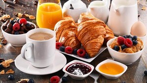 Una mesa de desayuno con croissants, frutos rojos, café y jugo.