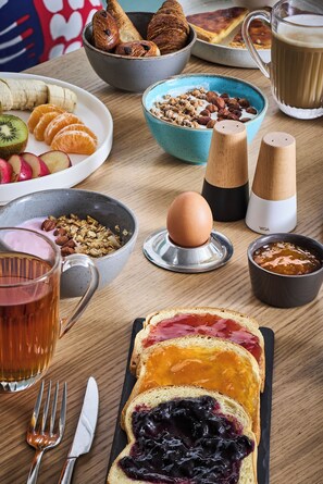 Een ontbijttafel met diverse etenswaren, zoals toast met jam, een kom ontbijtgranen, een bord fruit en een kop thee.