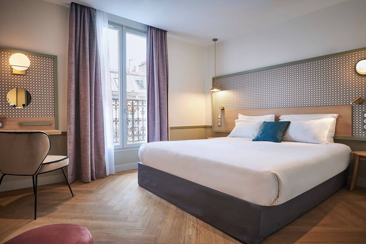 Een hotelkamer met een groot bed, een stoel, een bureau en een raam met gordijnen.