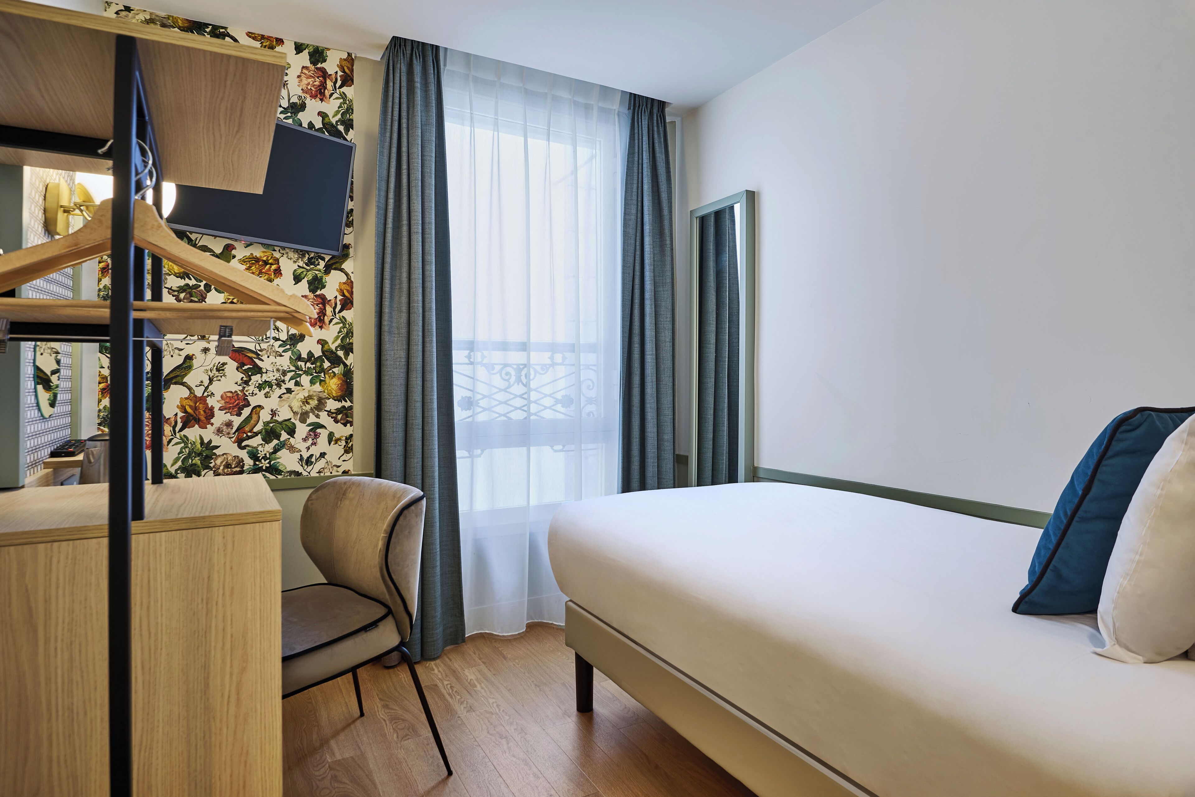 A hotel room with a bed, a desk, a chair, and a wardrobe.