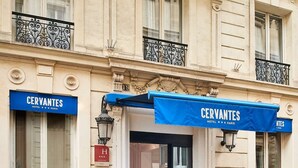 La façade d’un hôtel ornée de balcons en fer forgé, surmontée d’une marquise bleue et portant une enseigne indiquant « HÔTEL CERVANTES PARIS ».