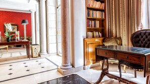 A spacious lobby with a marble floor, a large bookshelf, a glass-top desk, and a plush armchair. - Hotel Regence Paris (Paris)