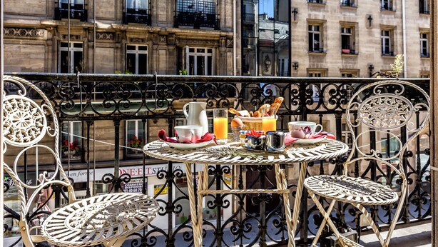A balcony with a round table and two chairs, featuring breakfast items like eggs, toast, and juice. - Hotel Regence Paris (Paris)