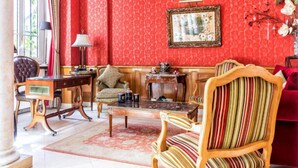 A room with a red patterned wallpaper, a wooden coffee table, a striped armchair, a sofa, and a framed picture on the wall. - Hotel Regence Paris (Paris)