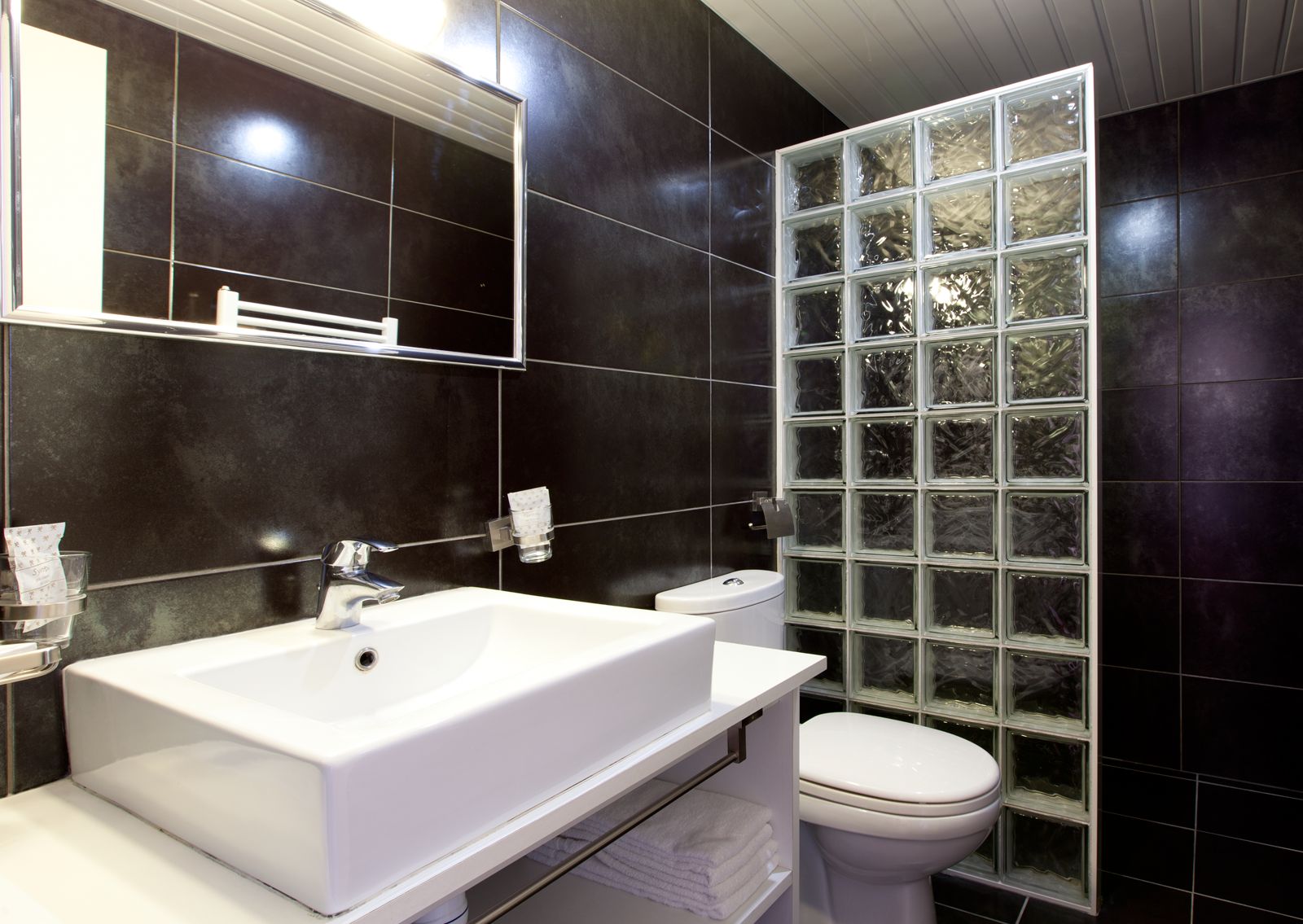 Un baño moderno con un lavamanos, espejo y retrete blancos.