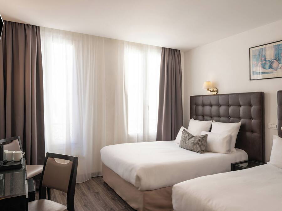 Habitación de hotel con dos camas, un escritorio, una silla, una lámpara y un cuadro en la pared.