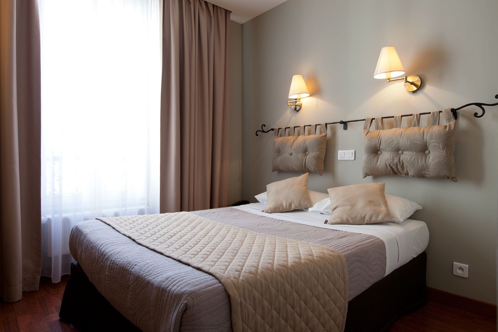 Ein Hotelzimmer mit einem großen Bett, zwei Wandlampen und Blick ins Freie.