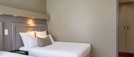 A hotel room with two beds, a nightstand, and a wardrobe.