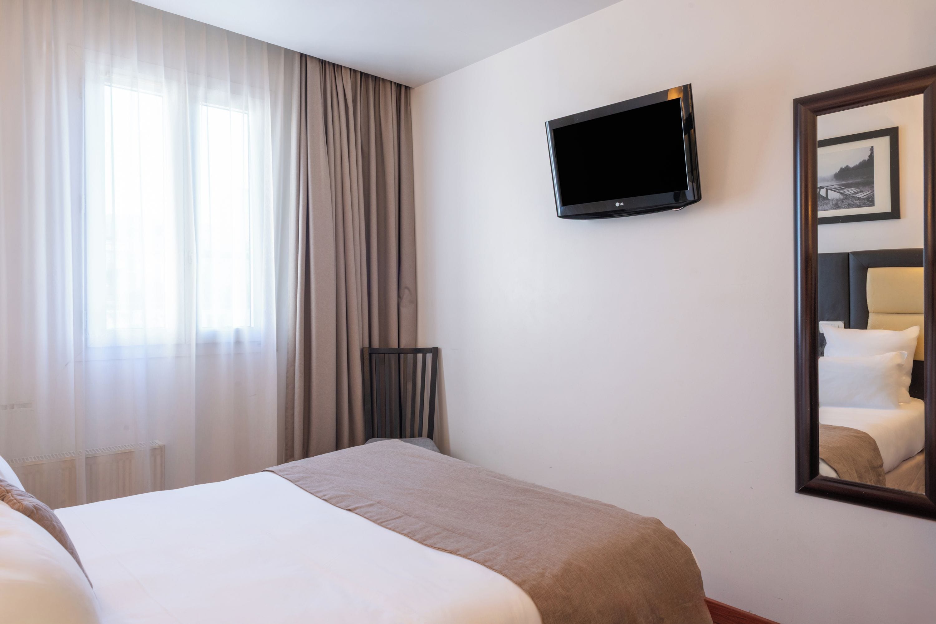 Una habitación de hotel con una cama, un televisor montado en la pared y un espejo grande que refleja la cama y un marco de fotos.