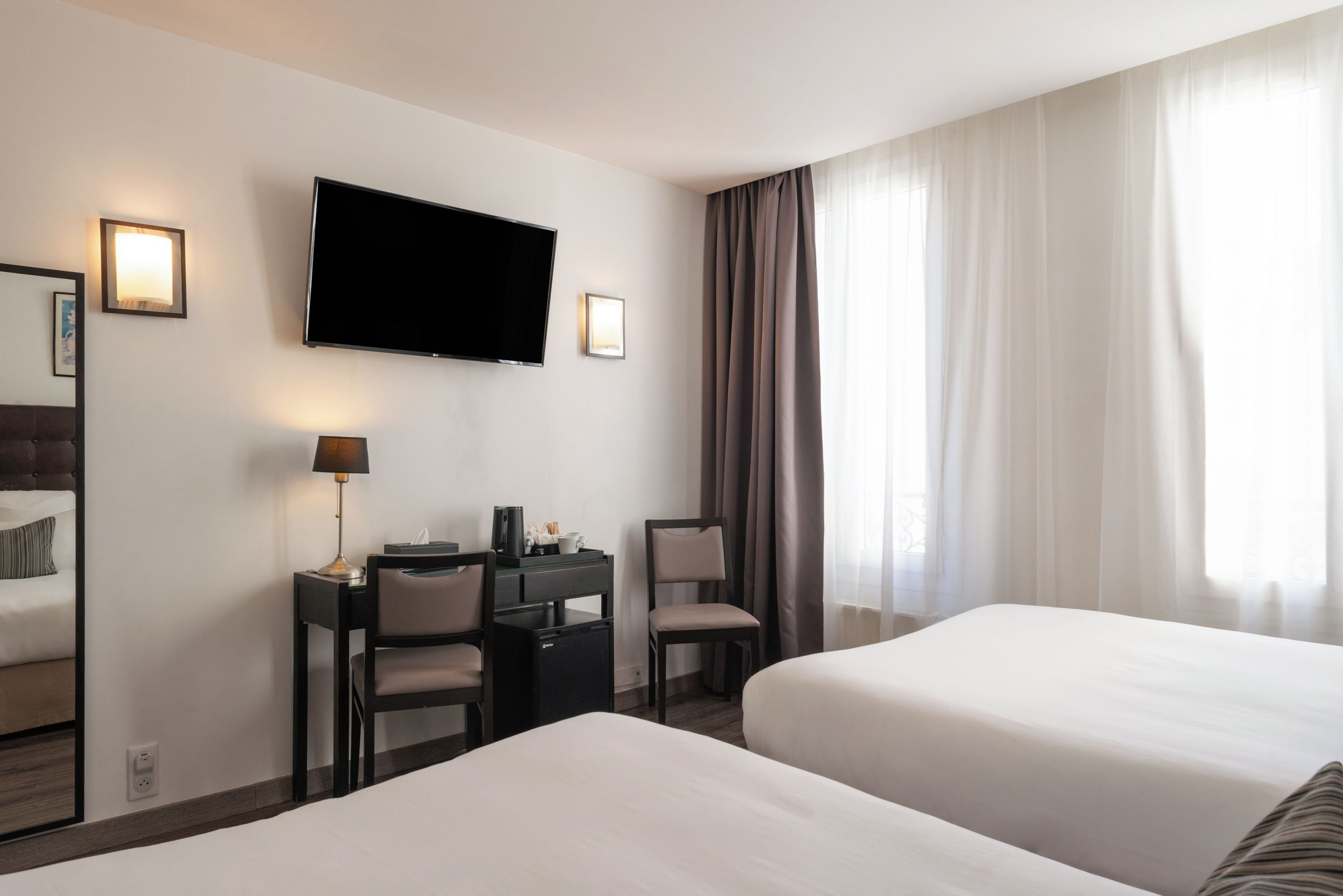 A hotel room with two beds, a desk with a chair, a television, and a window with curtains.