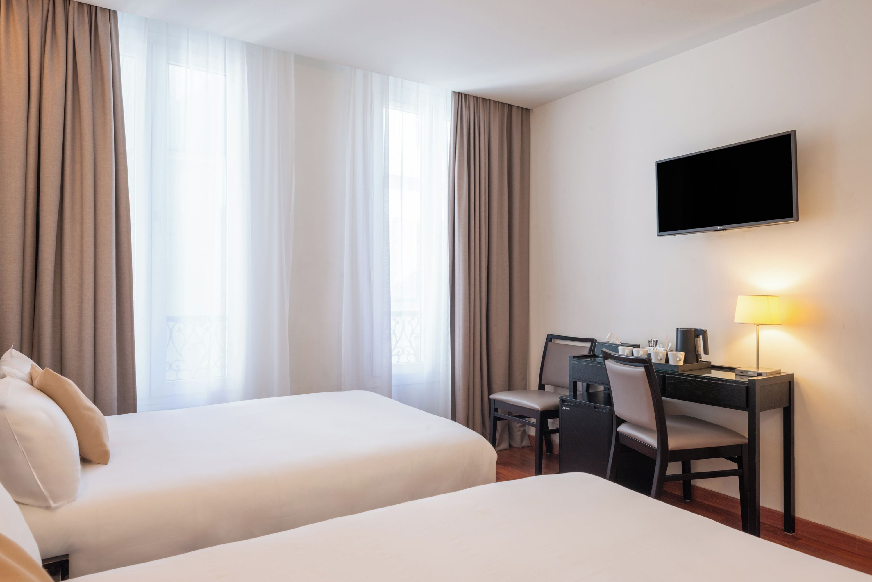 A hotel room with two beds, a desk with a chair, a television, and a coffee machine.