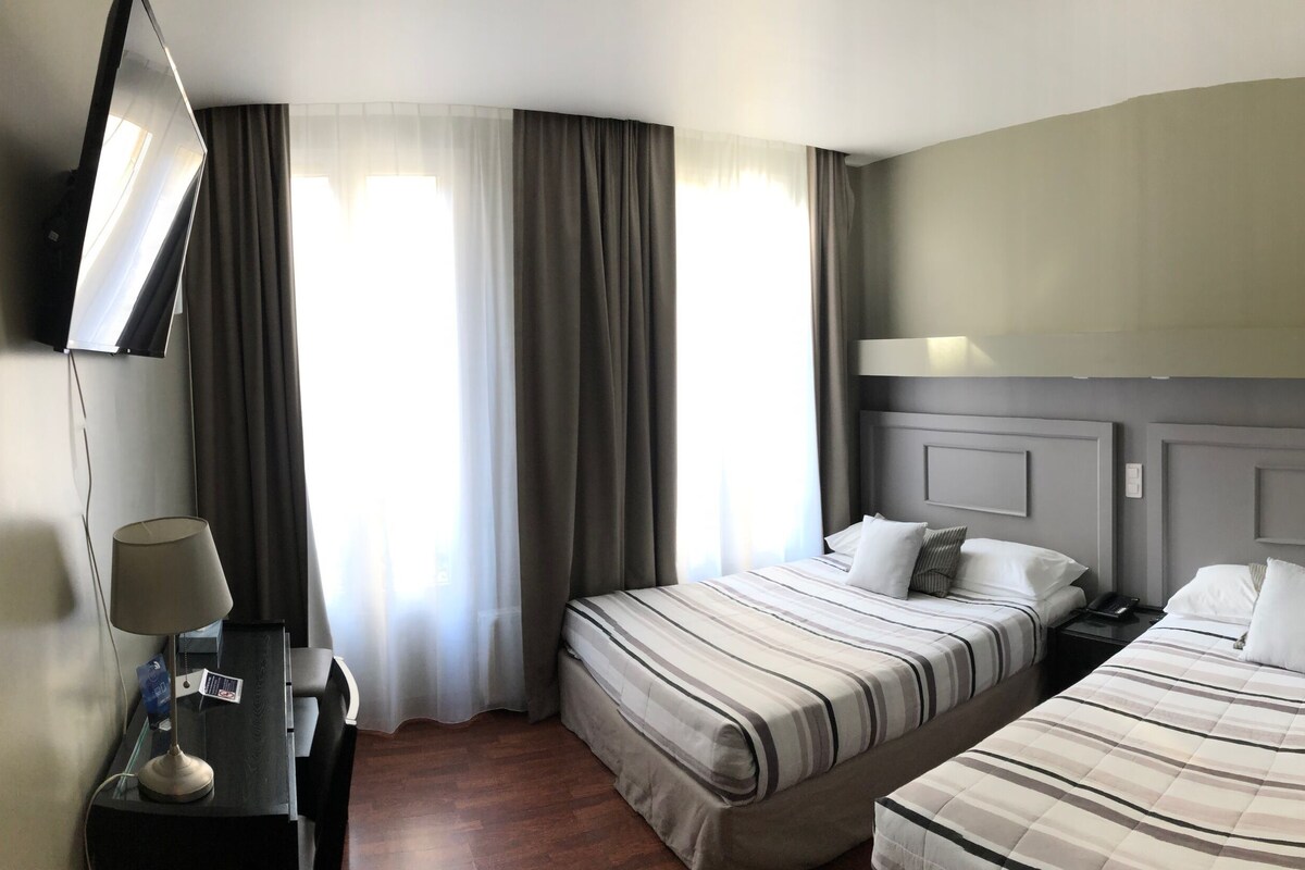 A hotel room with two beds, a desk, and a chair.