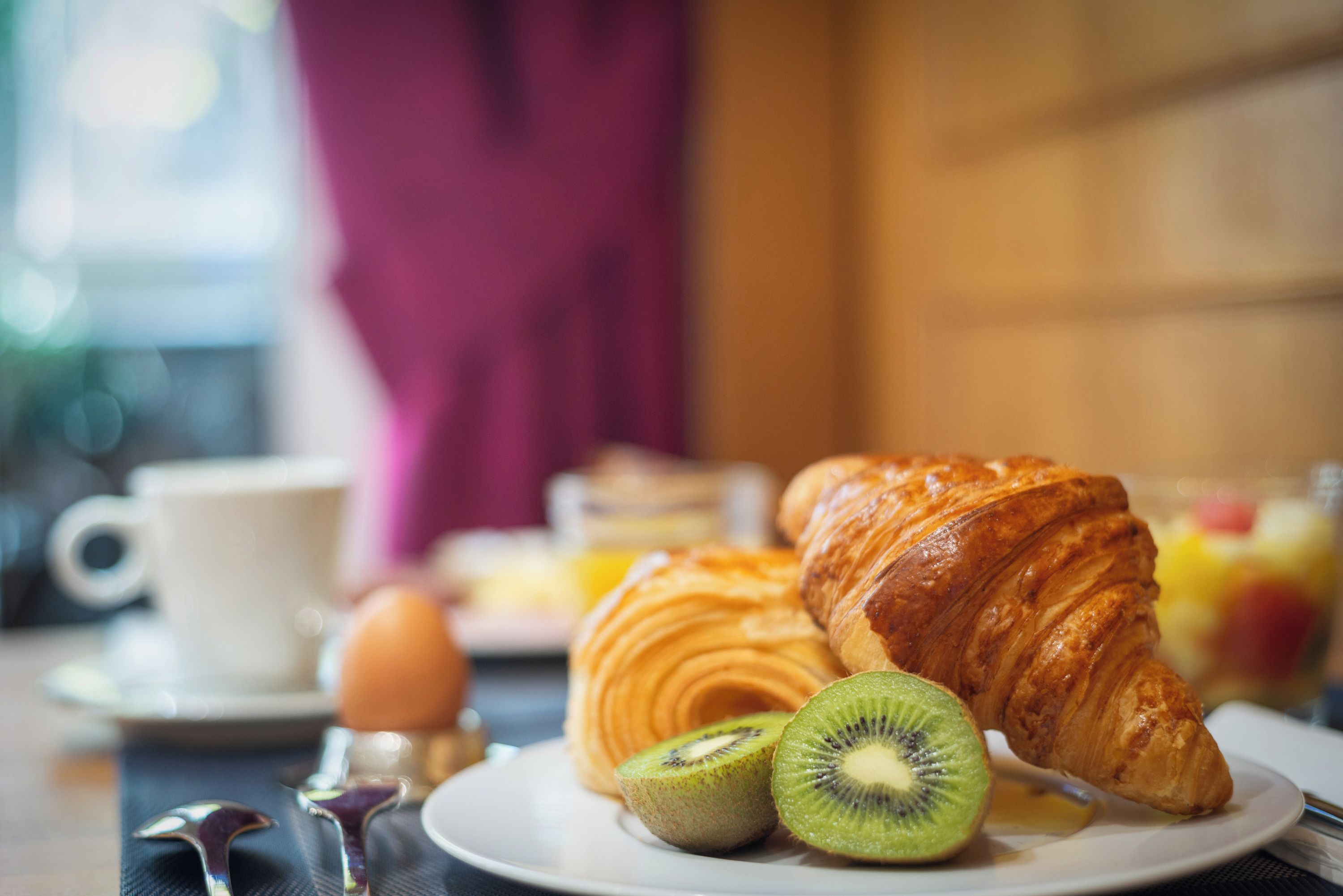 A breakfast setting with a croissant, kiwi halves, and a cup on a table.