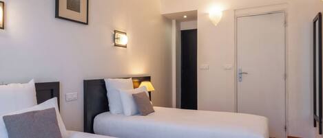 A hotel room with two beds, a framed picture on the wall, a door, and a light fixture.