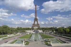 La Tour Eiffel à Paris, sous un ciel dégagé, entourée de verdure et d’un parc bien entretenu.