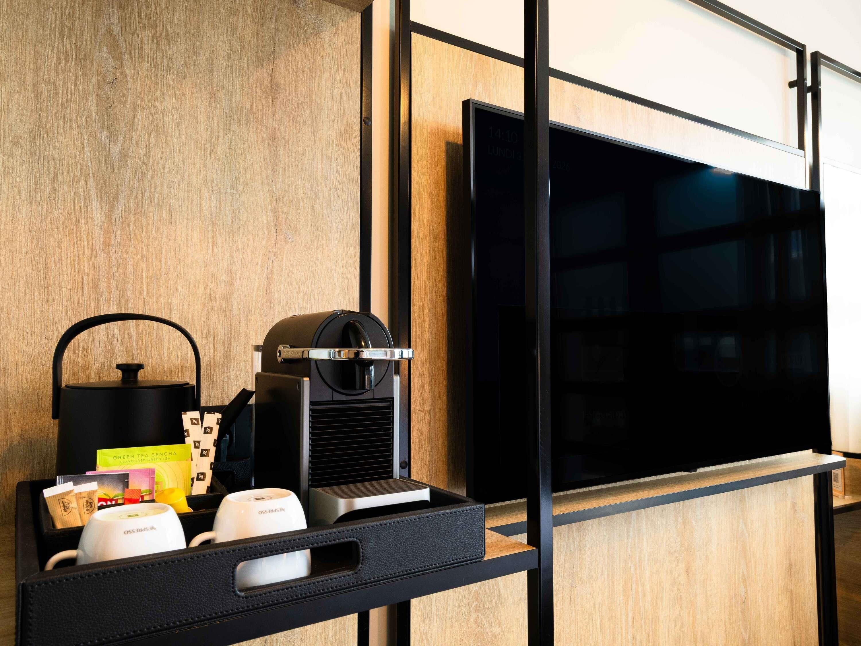 Una habitación moderna con televisión de pantalla plana montada en una pared de madera, una cafetera y un hervidor sobre una bandeja negra.