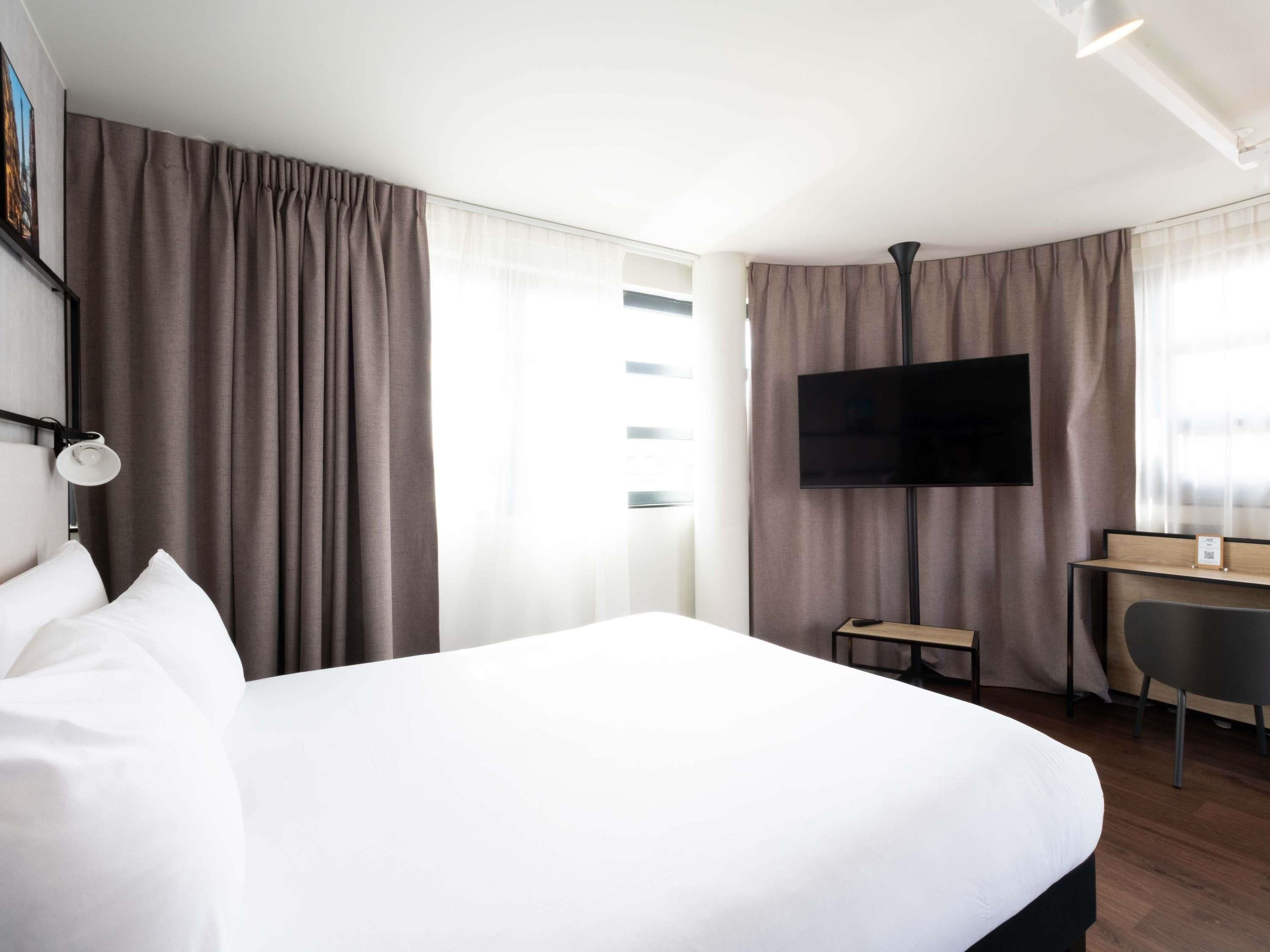 A hotel room with a bed, a desk, a chair, a TV, and curtains.
