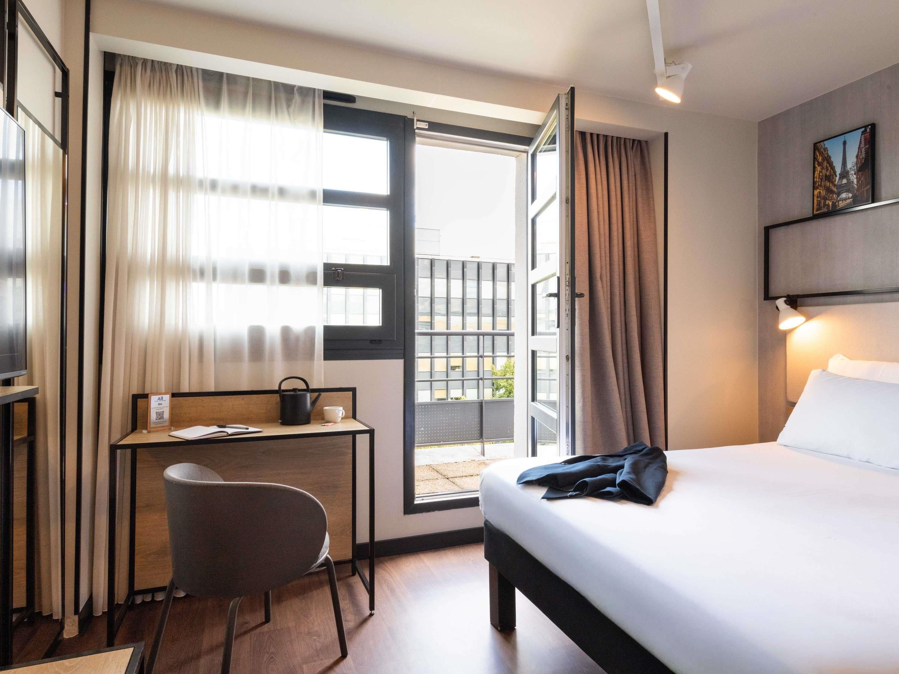 Una habitación de hotel con una cama, un escritorio con una silla, una ventana con cortinas y vistas al exterior.