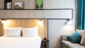 Une chambre d’hôtel avec un lit, un canapé, une petite table et des lampes fixées au mur.