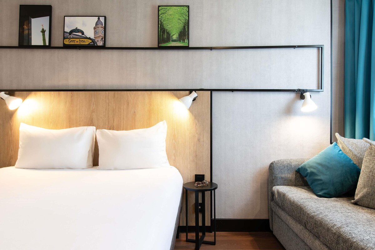 Une chambre d’hôtel avec un lit, un canapé, une petite table et des lampes fixées au mur.