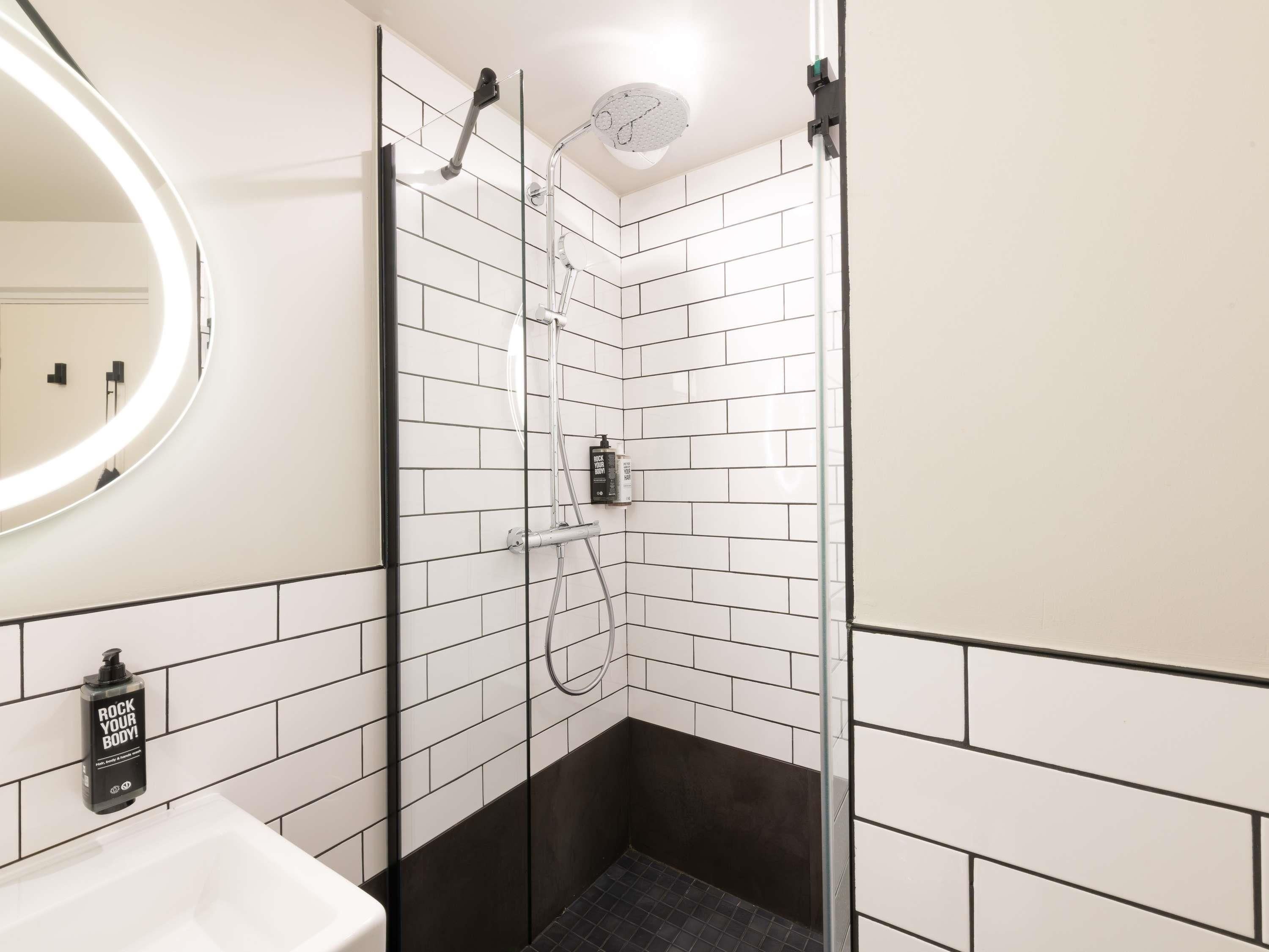 A modern bathroom with a glass shower enclosure, a white sink, and a black soap dispenser.
