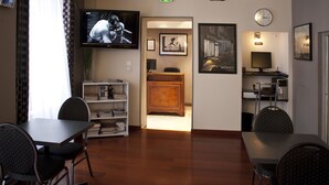 A hotel room with a TV, a wooden desk, a bookshelf, and a dining area with chairs. - Hotel Hippodrome (Paris)