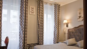 A hotel room with a bed, a bedside table, a lamp, and a window with curtains. - Hotel Hippodrome (Paris)