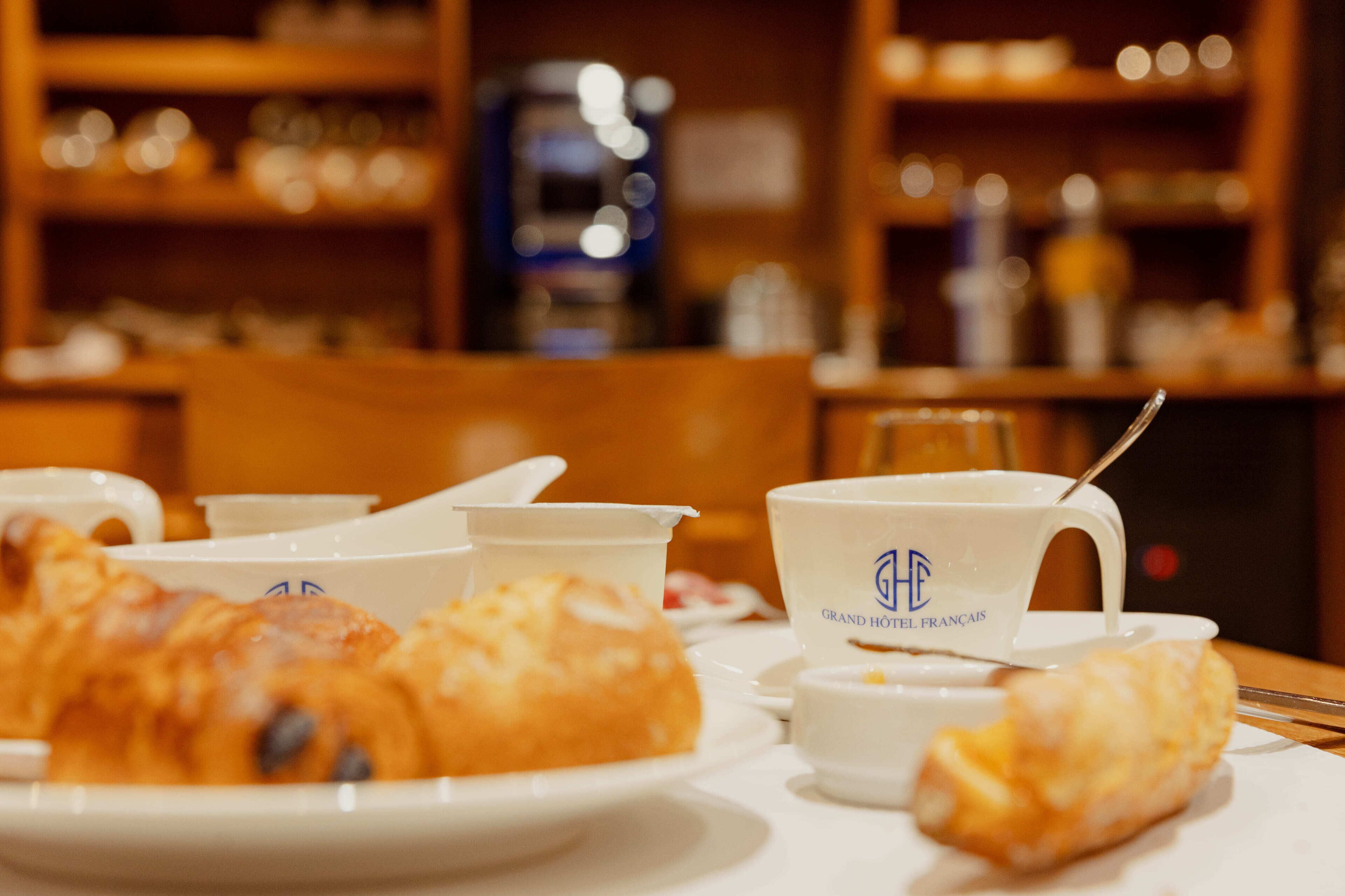 A table with croissants, coffee cups, and a teapot, suggesting a breakfast setting.
