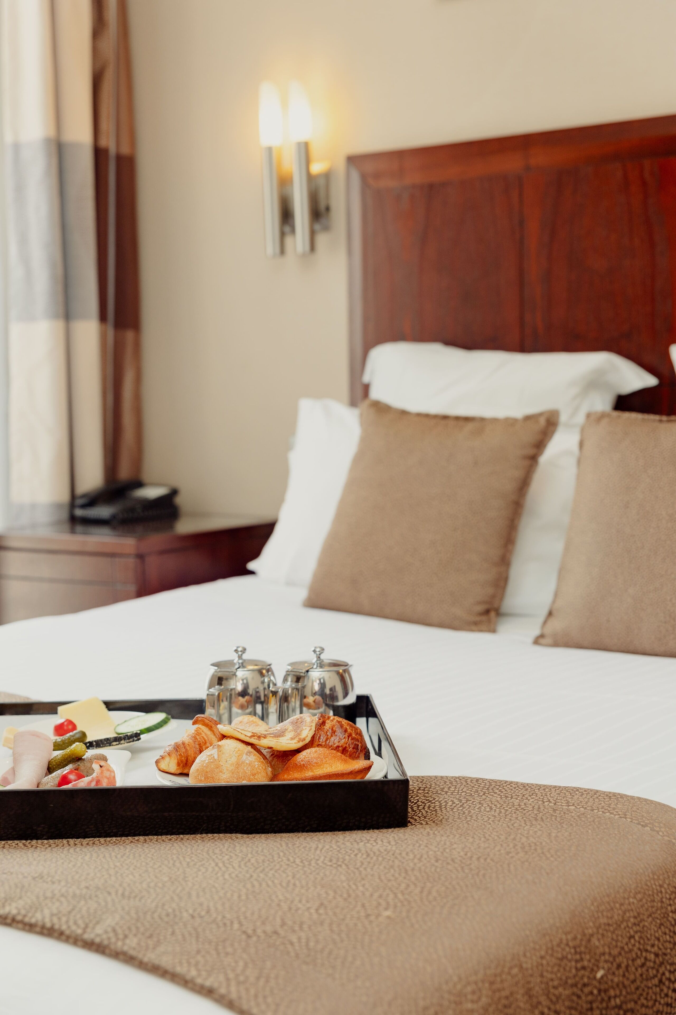 Une chambre d’hôtel avec un lit soigneusement fait, un plateau de petit-déjeuner et une table de chevet avec une lampe.