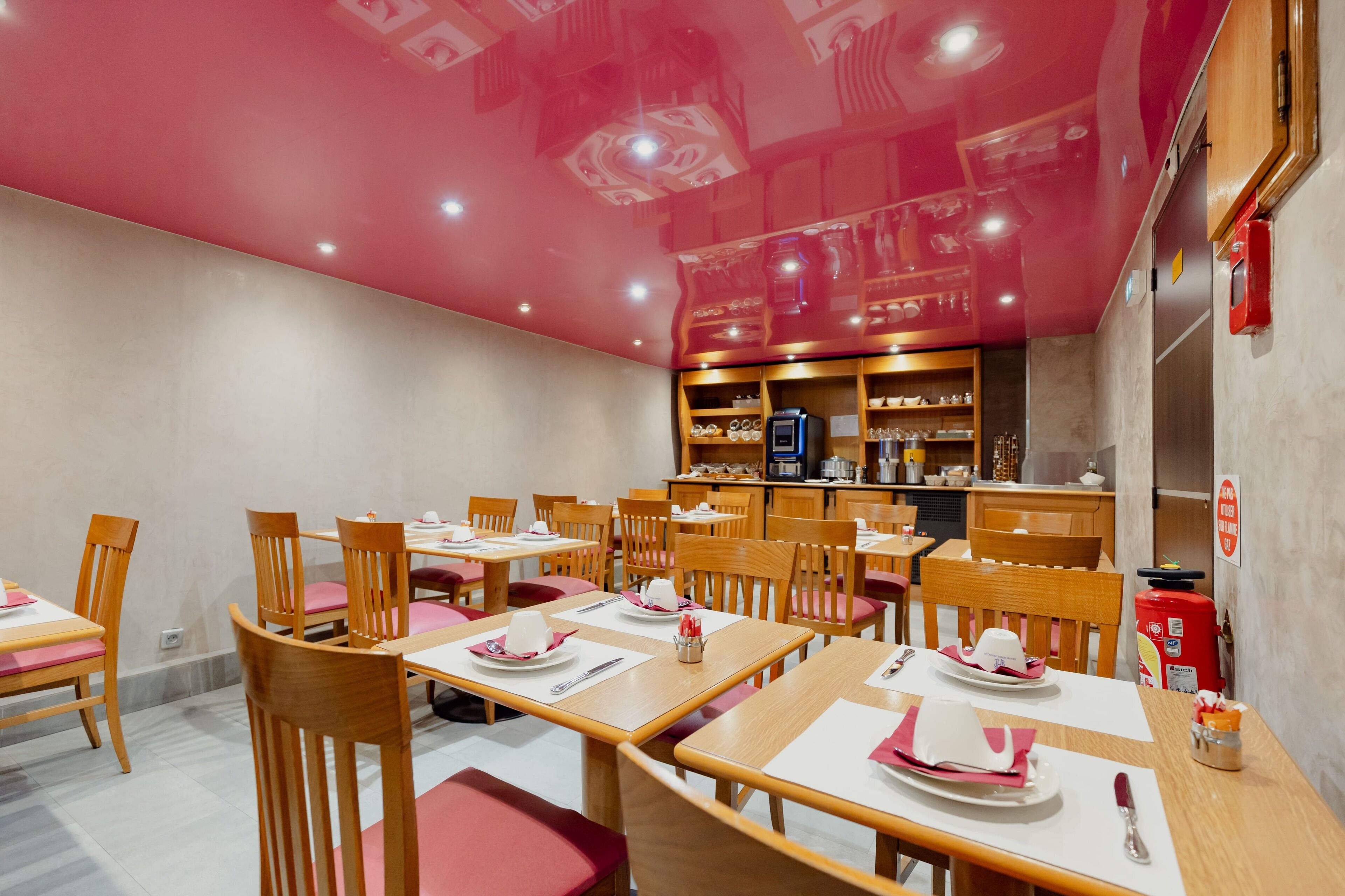 Un restaurante con mesas y sillas de madera, una barra con distintos artículos, y un techo rojo.