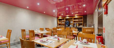 Un restaurante con mesas y sillas de madera, una barra con distintos artículos, y un techo rojo.