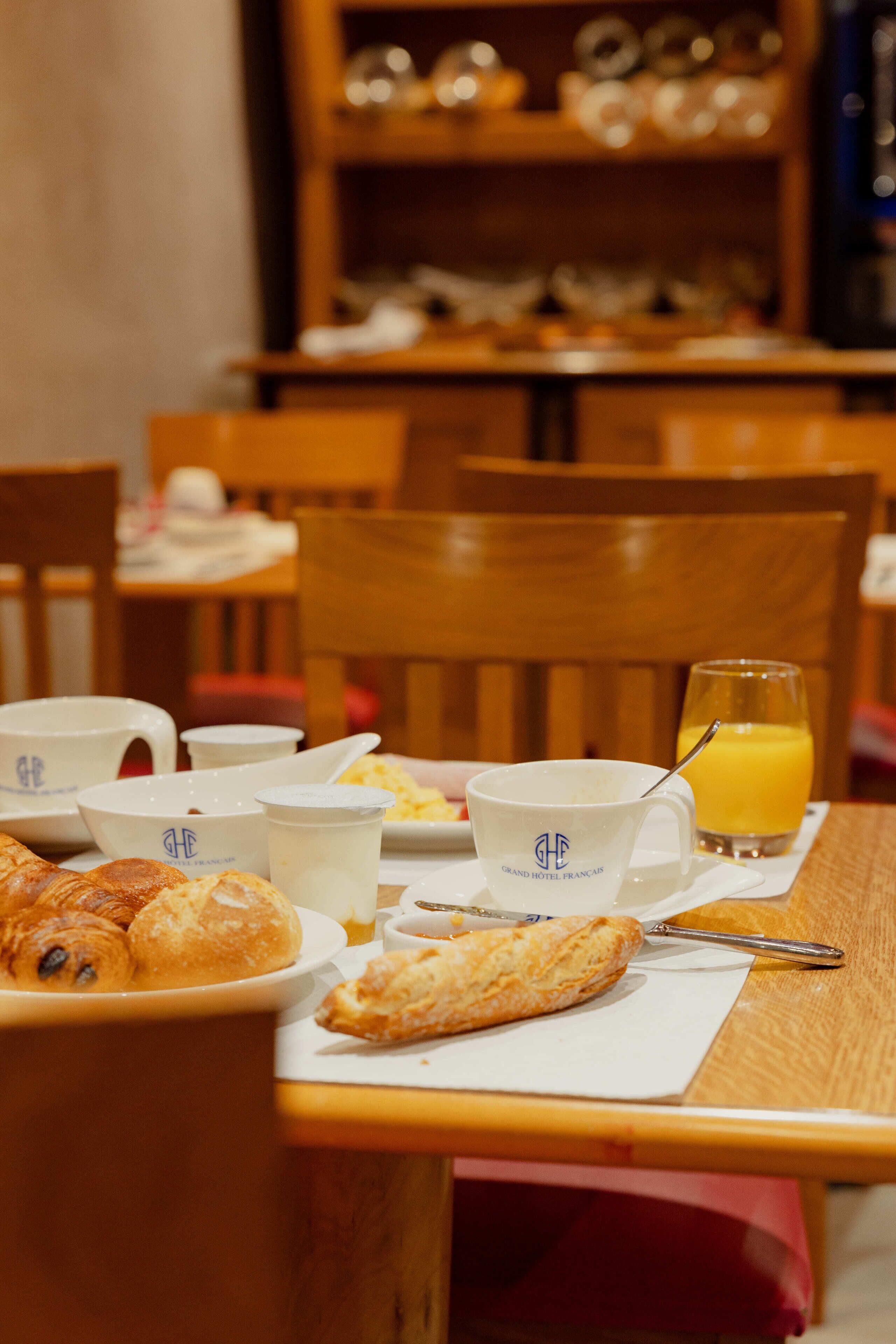 A breakfast table with croissants, a glass of orange juice, and coffee cups.