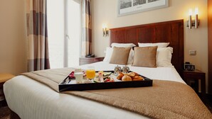 A hotel room with a neatly made bed, breakfast tray with croissants, juice, and a coffee pot. - Grand Hotel Francais (Paris)