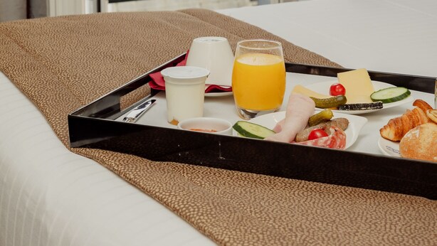 A breakfast tray with croissants, cheese, tomatoes, and juice on a bed in a hotel room with a view of buildings through a glass door. - Grand Hotel Francais (Paris)