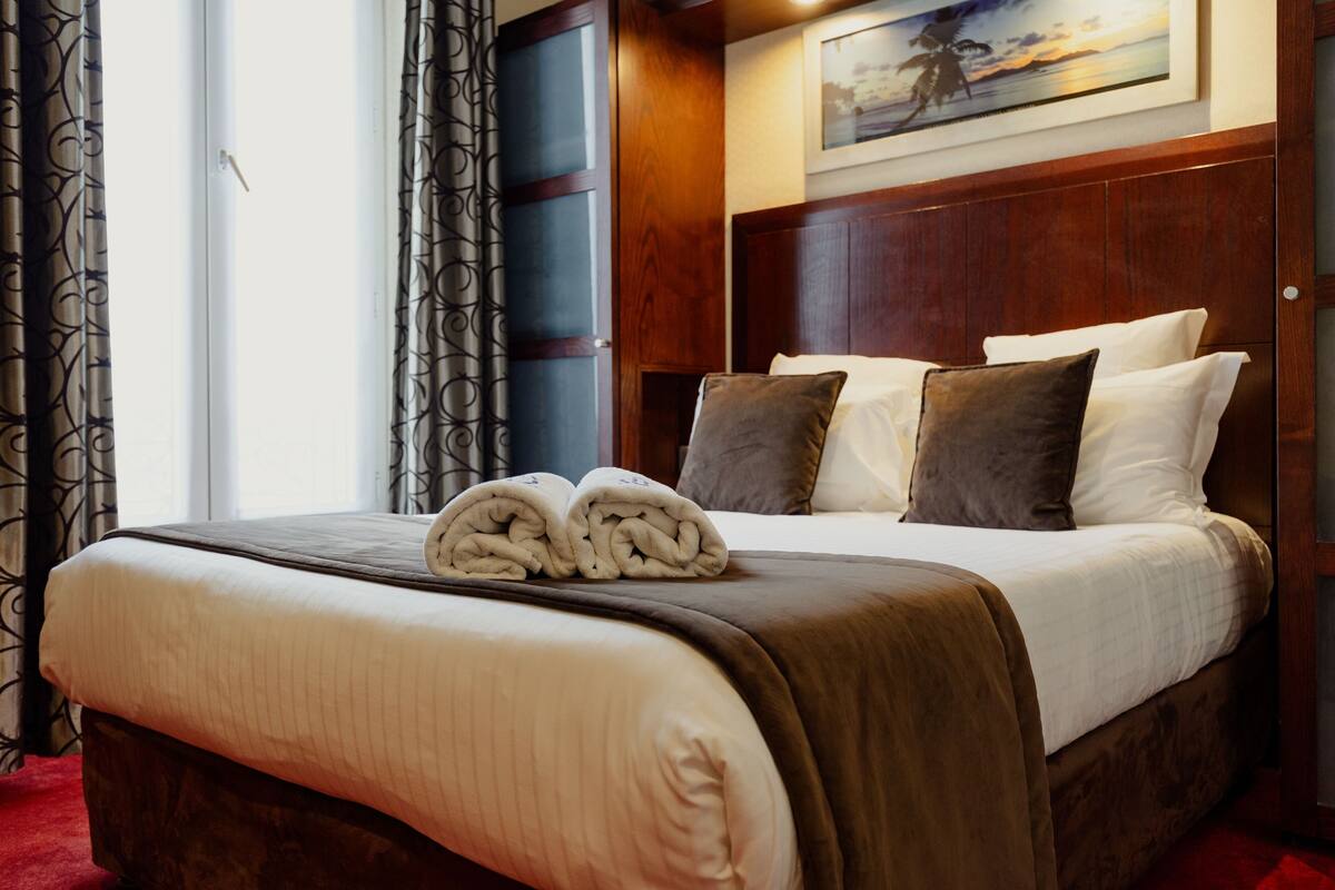 A neatly made bed with a brown headboard, white bedding, and two rolled towels.