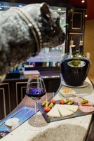 A bar counter with a glass of red wine, a bottle of champagne, cheese, and various snacks.