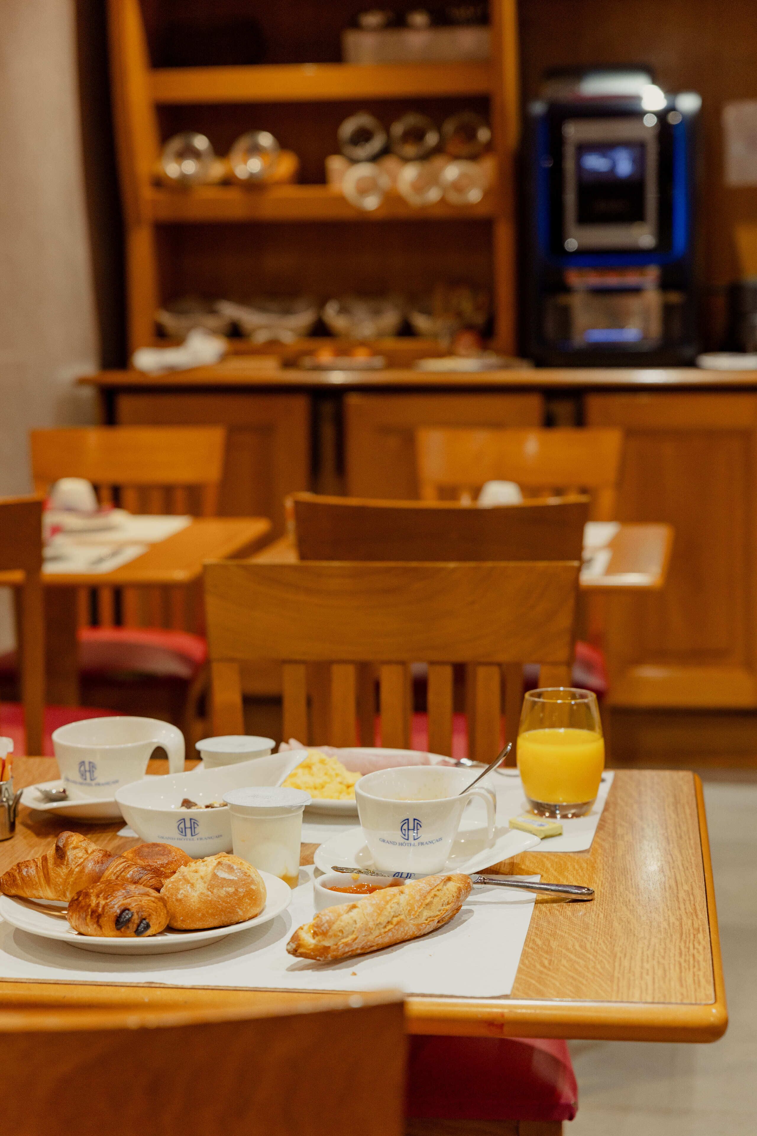 A breakfast setting with croissants, coffee cups, and a glass of orange juice on a table.