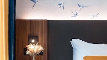 A hotel room with a bed, a nightstand with a vase, and a wall mural of birds.