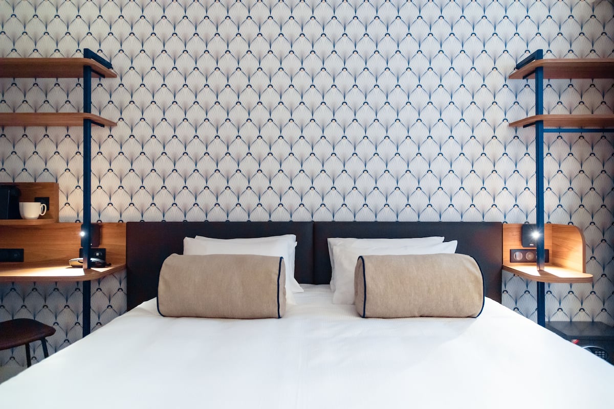 Una habitación de hotel con una cama bien hecha, dos mesitas de noche con lámparas y un papel tapiz estampado.