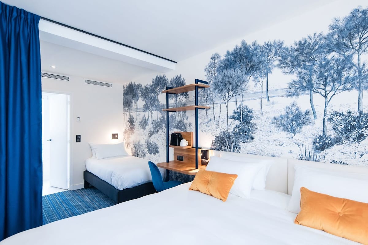 Habitación de hotel con dos camas, un sofá, una estantería de madera y un mural de un paisaje nevado.