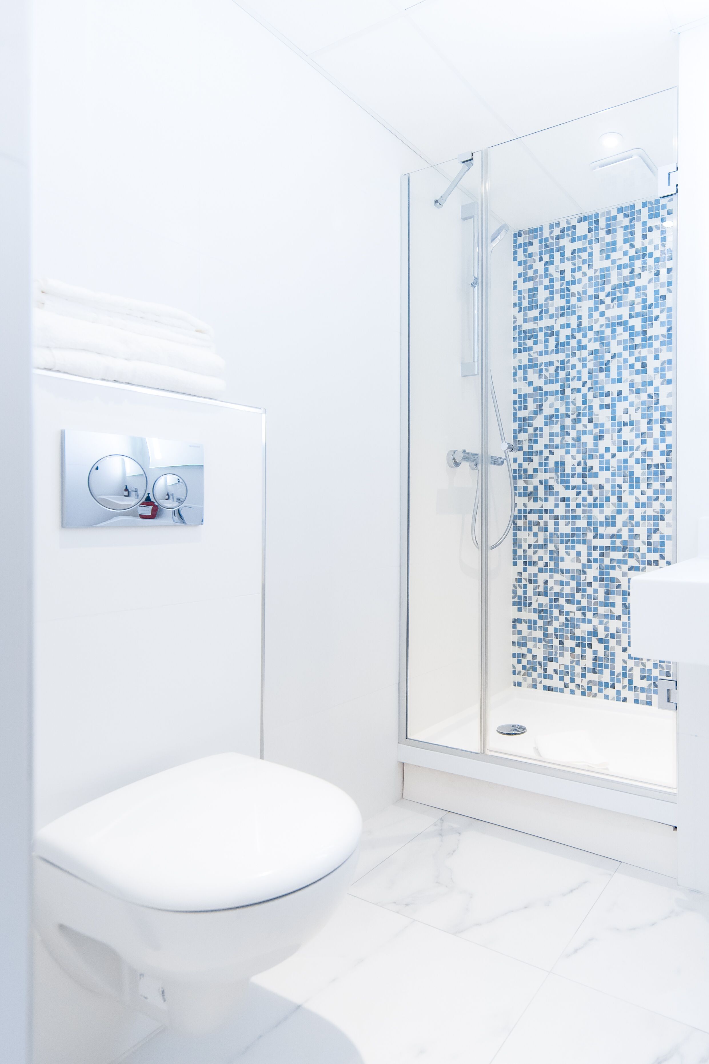 A modern bathroom with a glass-enclosed shower, a white toilet, and a sink with a blue mosaic tile backsplash.