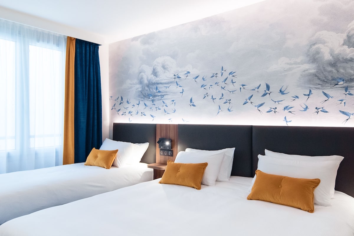 Habitación de hotel con dos camas, un mural de pájaros y un reloj en la pared.