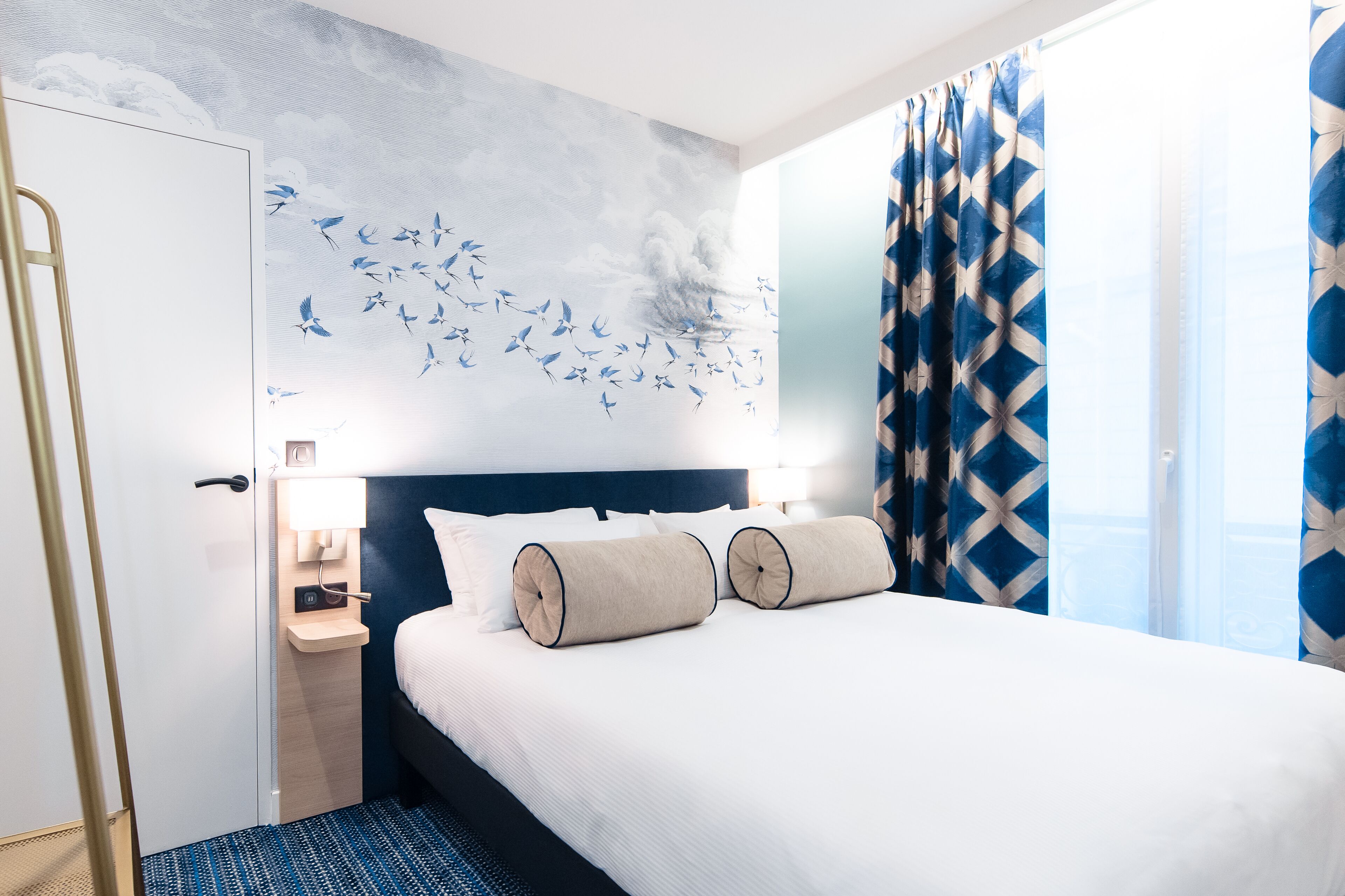 Una habitación de hotel con cama, mesita de noche, un mural en la pared y cortinas.