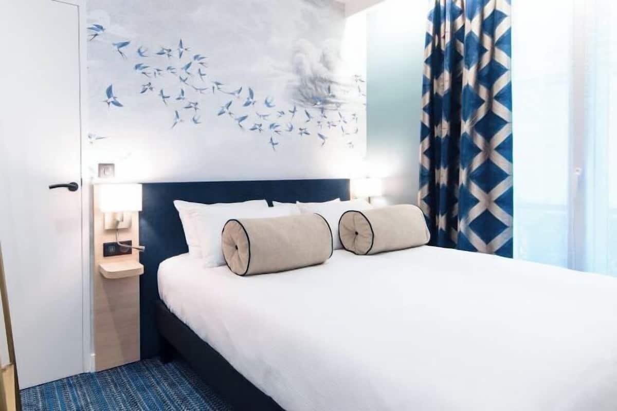 Una habitación de hotel con una cama, una mesita de noche, un mural en la pared y una cortina estampada.