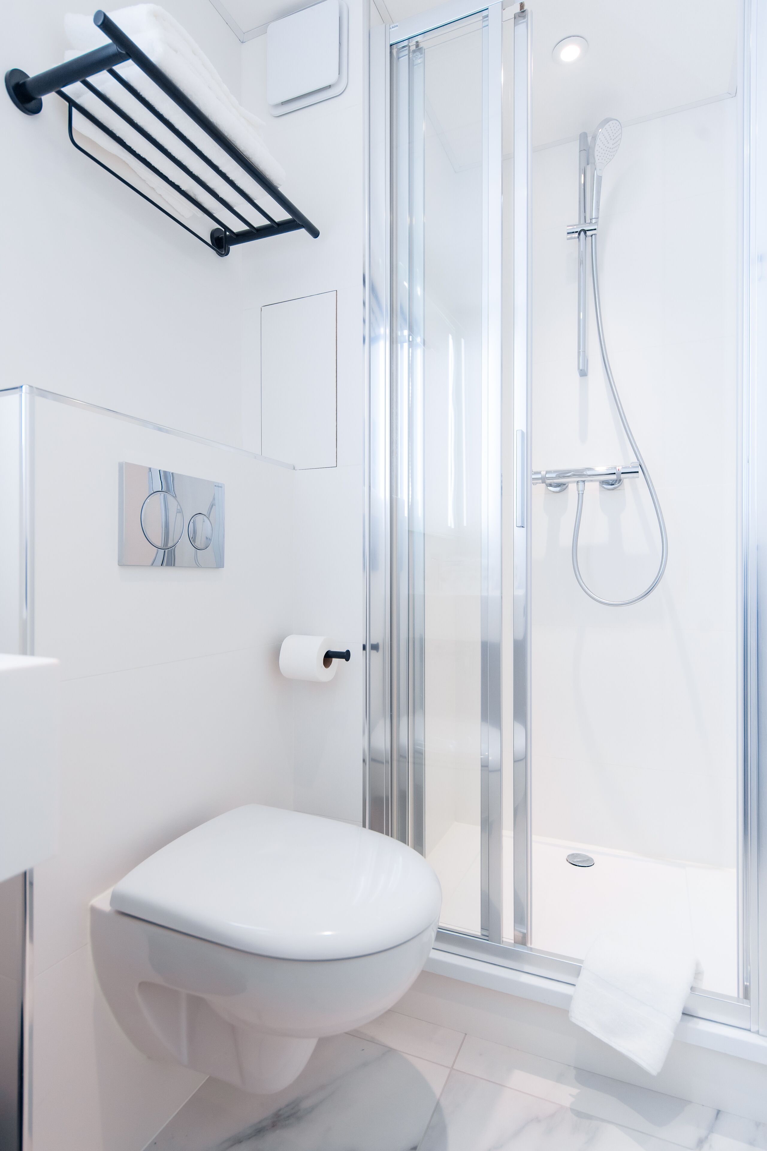 A modern bathroom with a toilet, a glass shower enclosure, and a towel rack.