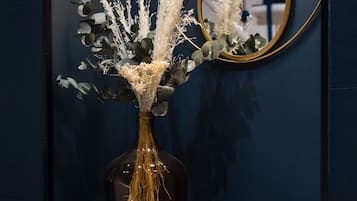 A dark blue cabinet with a glass vase containing white flowers and greenery, a round mirror with a sunburst design, and a light fixture above.