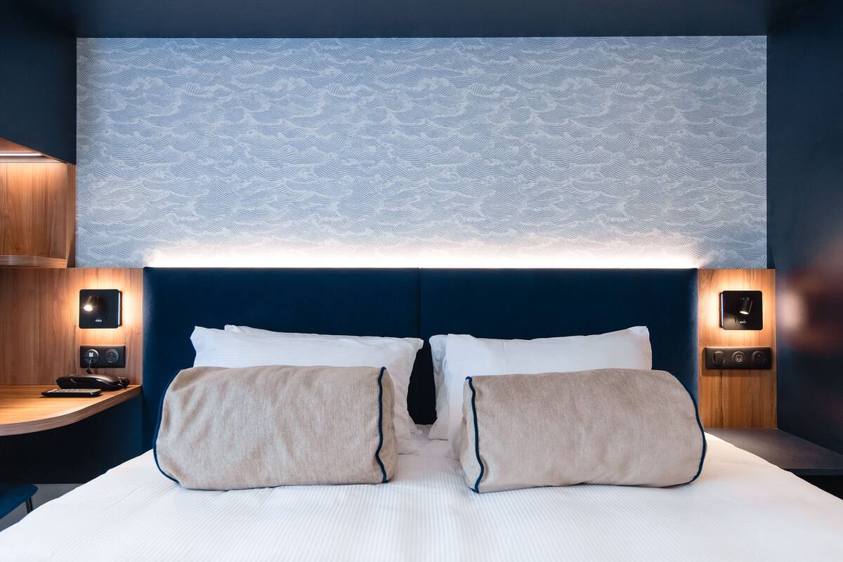 Habitación de hotel con una cama grande, dos mesitas de noche, un cabecero de madera y un papel tapiz estampado.