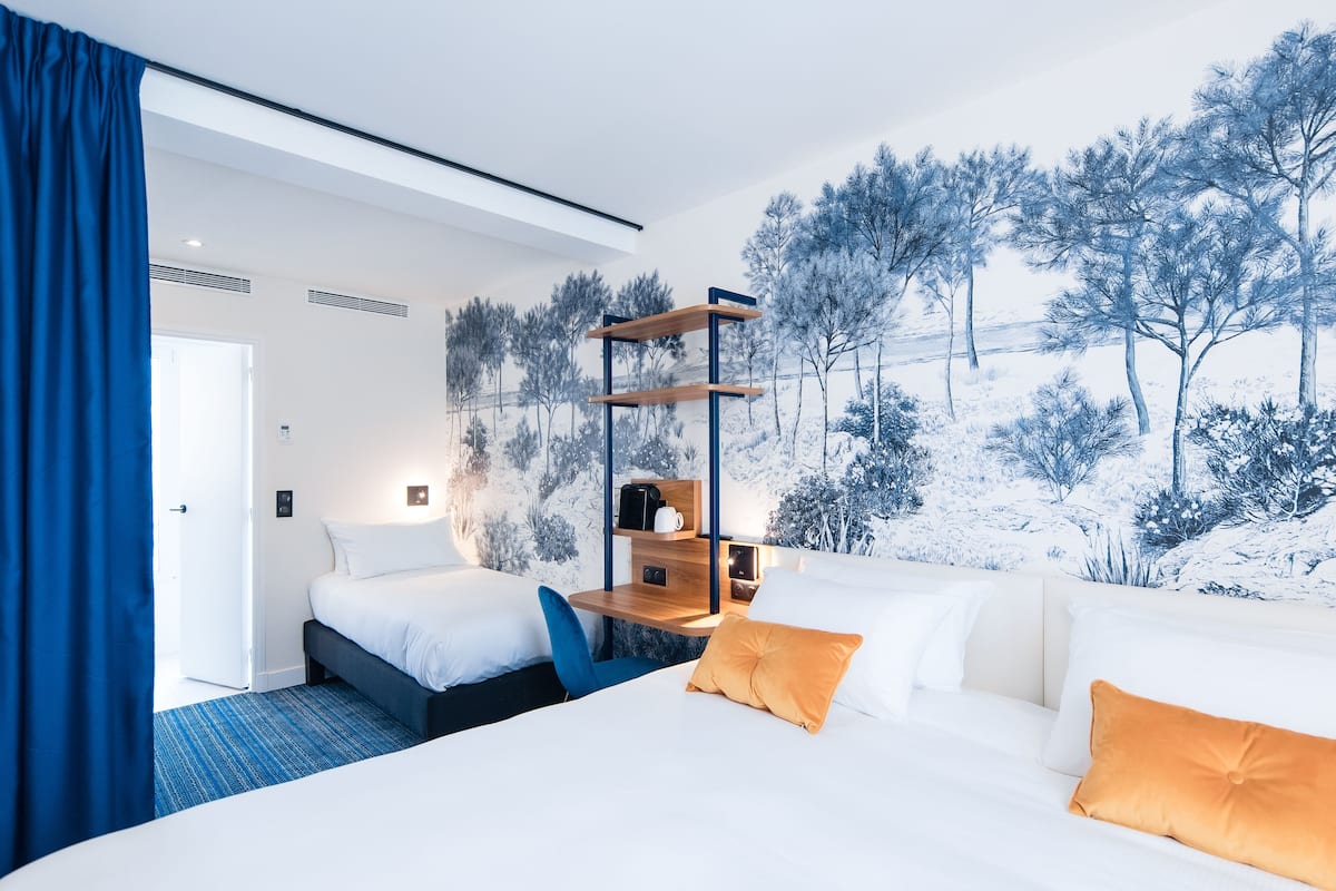 Habitación de hotel con dos camas, una estantería de madera y un mural de un paisaje nevado.